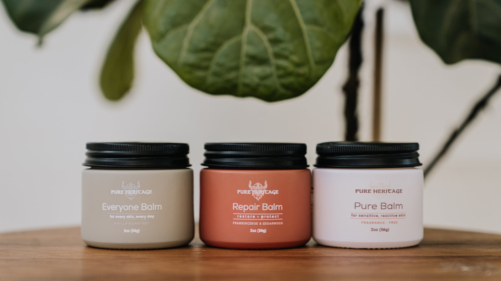 Three balm jars labeled 'Pure Balm', 'Repair Balm', and 'Everyone Balm' on a wooden surface with a plant in the background.