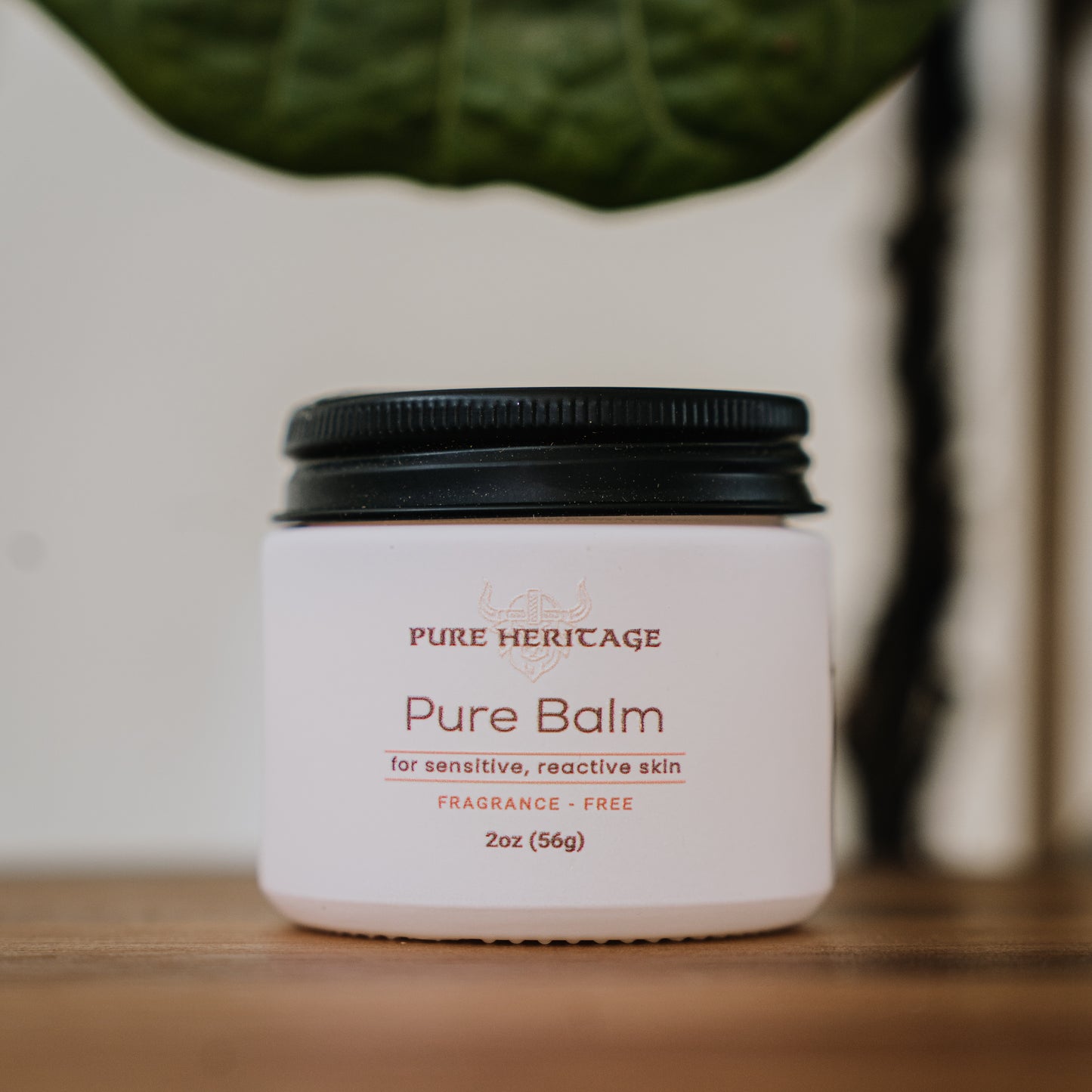 Jar of Pure Heritage Pure Balm on a wooden surface with a blurred plant in the background