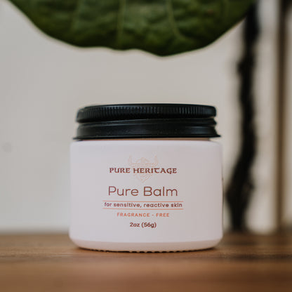Jar of Pure Heritage Pure Balm on a wooden surface with a blurred plant in the background